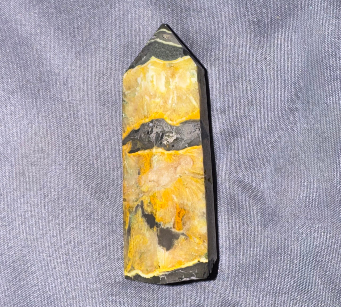 A natural pointed crystal mineral specimen with yellow, black, and white marbled patterns, displayed on a textured gray fabric background.