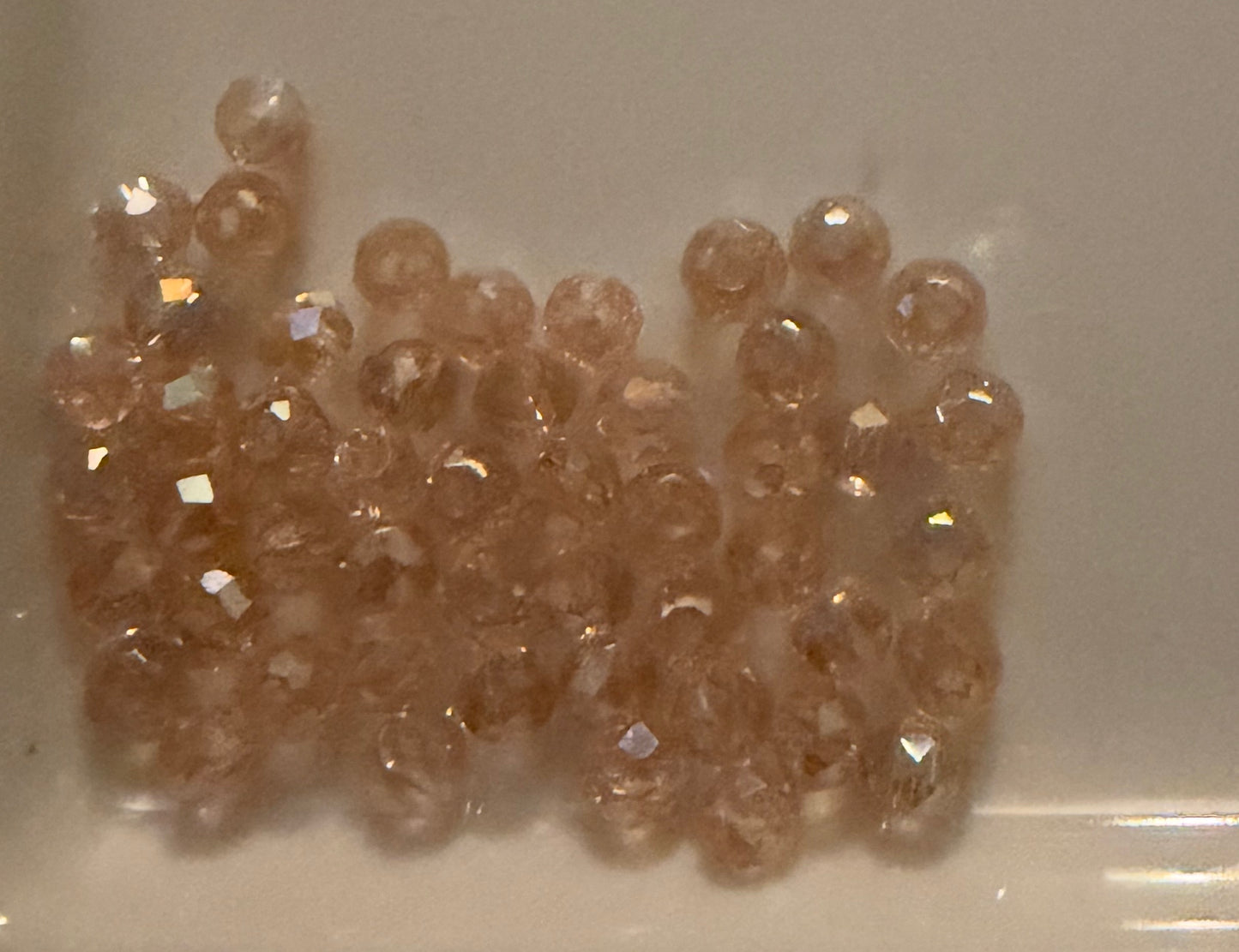 A pile of small, faceted round beads in a warm peachy-pink color, clustered together on a light beige surface.