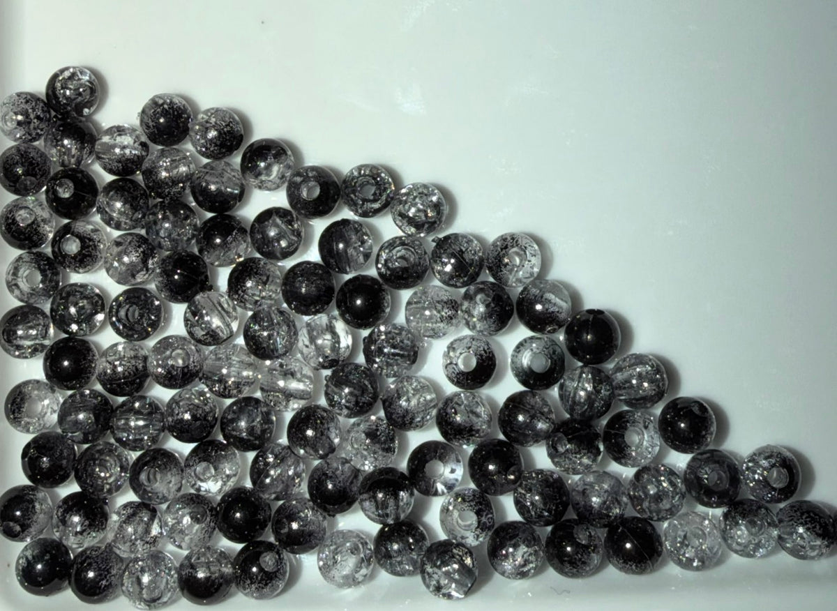 A pile of round, clear glass beads filled with black glitter, arranged on a plain white surface.