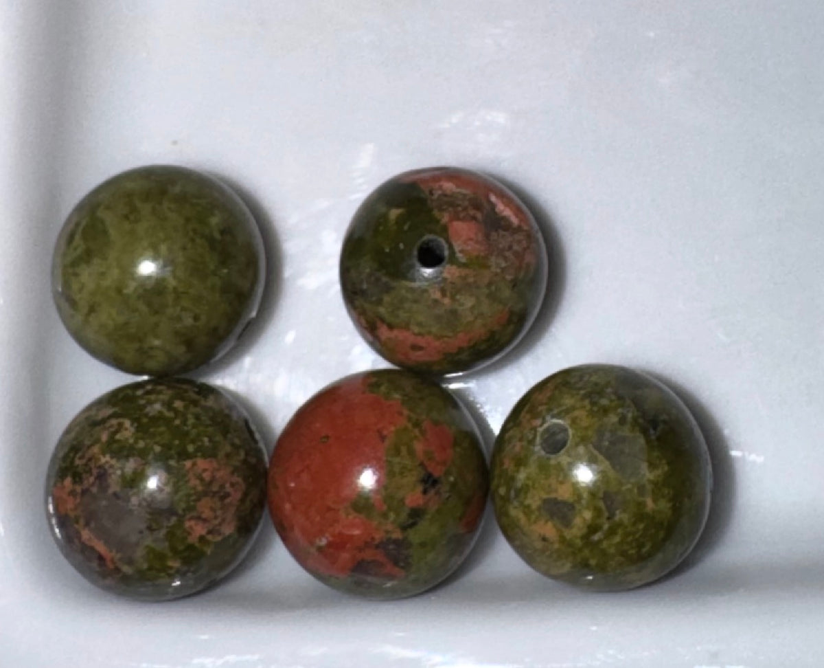 Five polished round gemstone beads with natural green and reddish-brown marbling, arranged on a white surface. Four beads have visible holes, indicating they are likely jewelry-making beads.