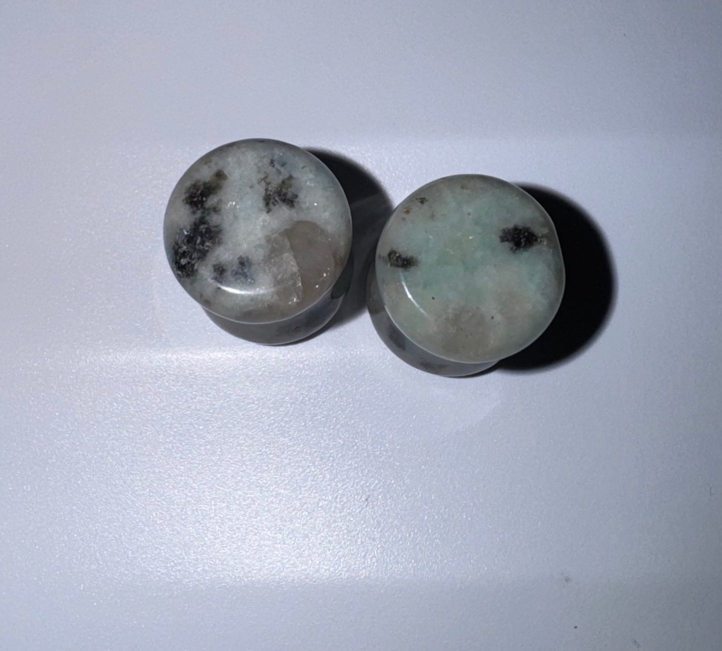 Two kiwi Jasper stone ear gauges with dark inclusions on a white background