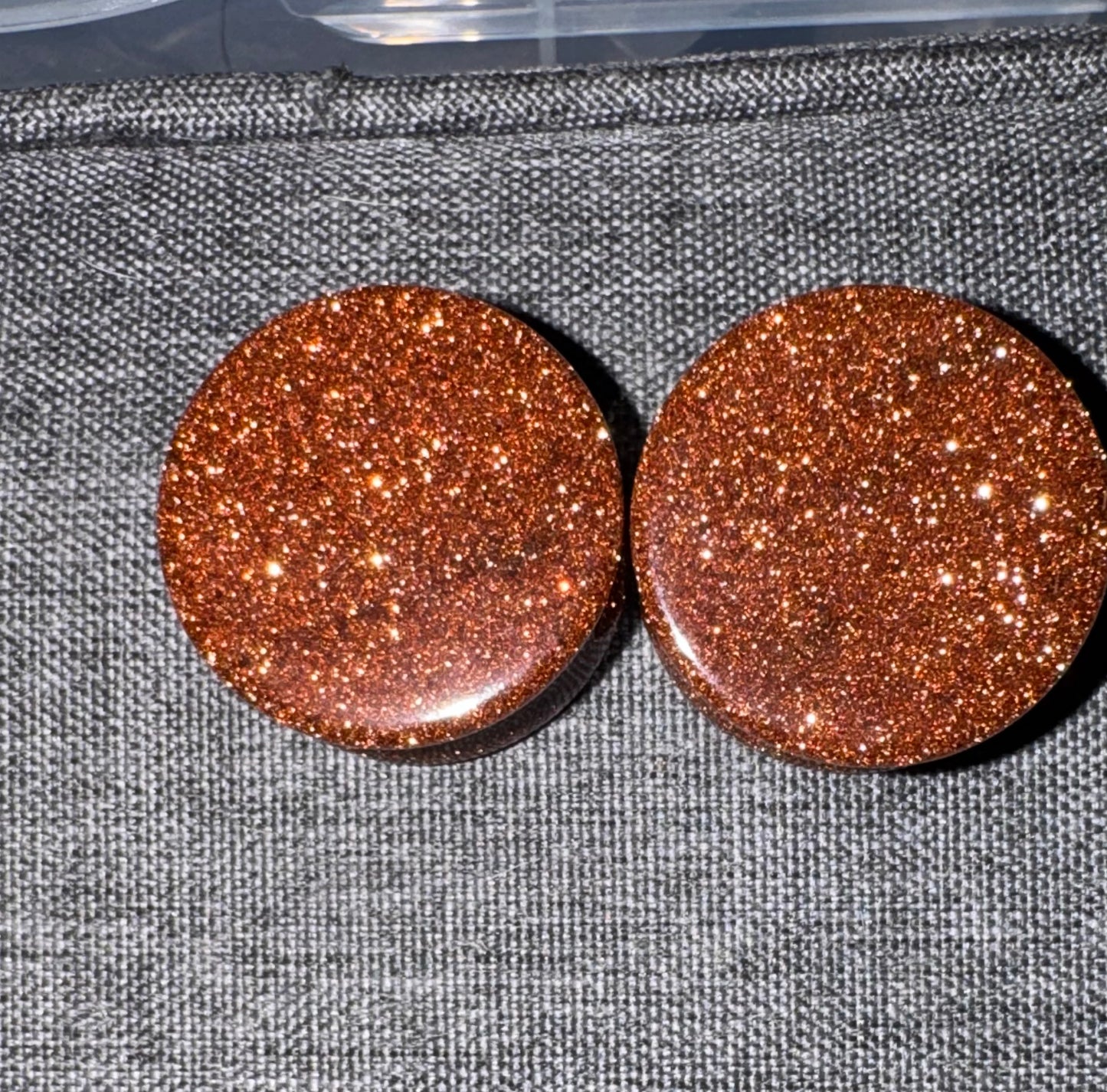 Pair of round, glittery brown earrings on a textured gray surface