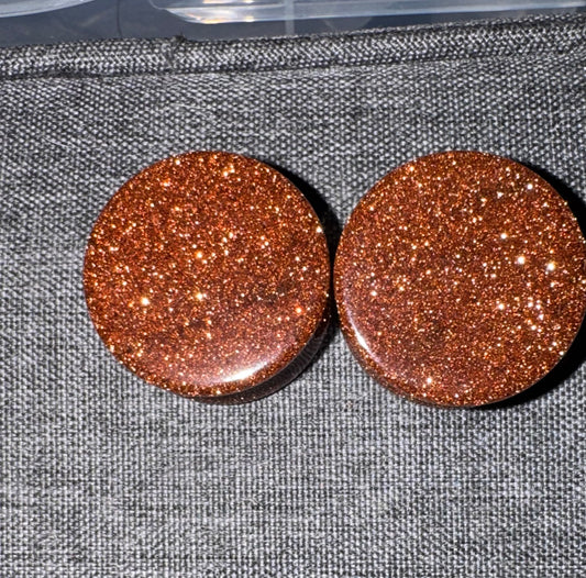 Pair of round, glittery brown earrings on a textured gray surface