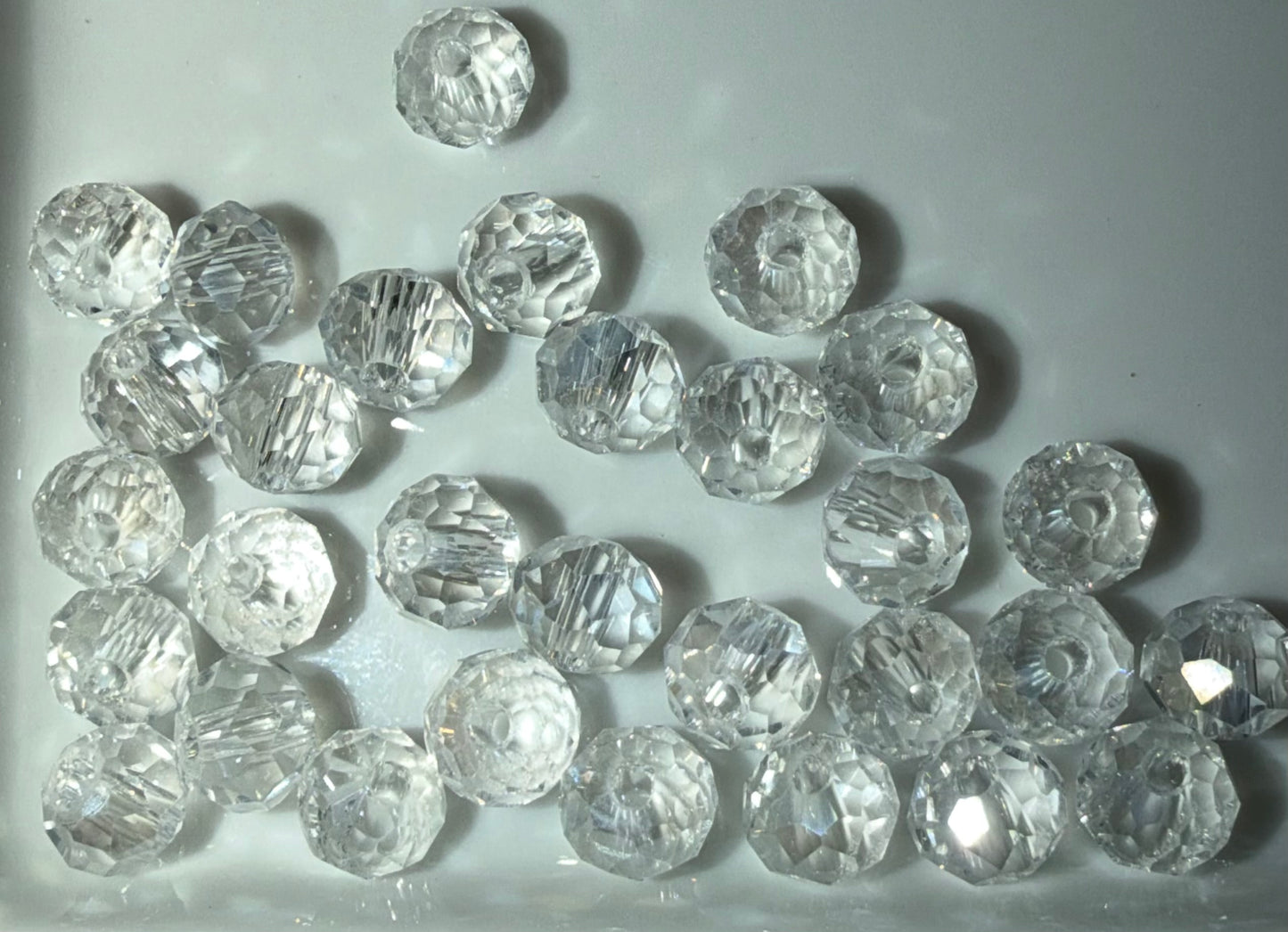 A group of clear, faceted round beads scattered on a light gray background.