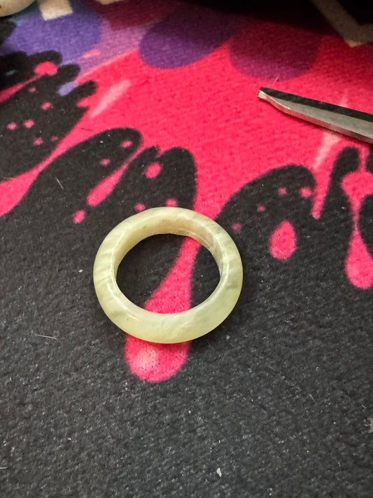 Jade ring on a black and pink textured surface with tweezers