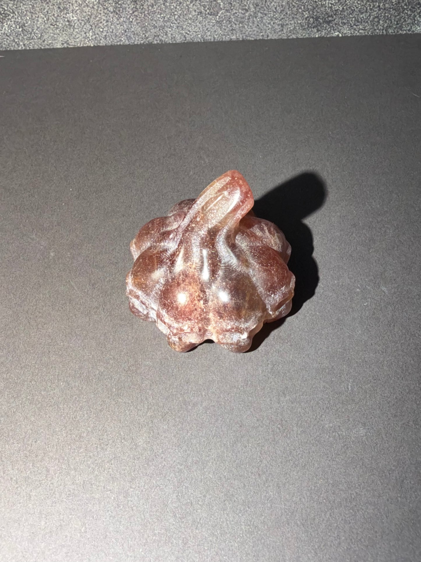 A small carved stone figurine resembling a stylized pumpkin or seed pod, shown on a dark gray surface with a cast shadow.