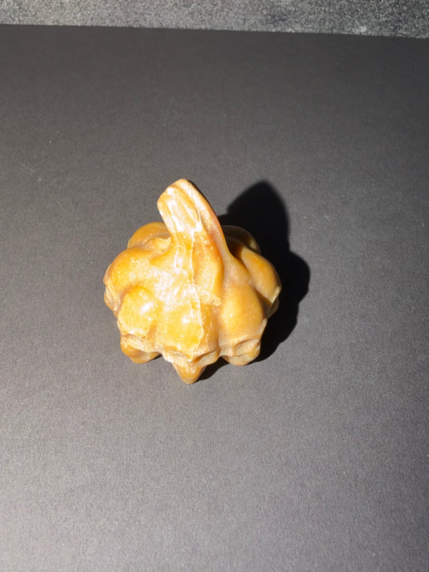 A small carved figurine of a rabbit in a warm golden-brown color, standing on a dark gray surface with a hard shadow cast to the right.