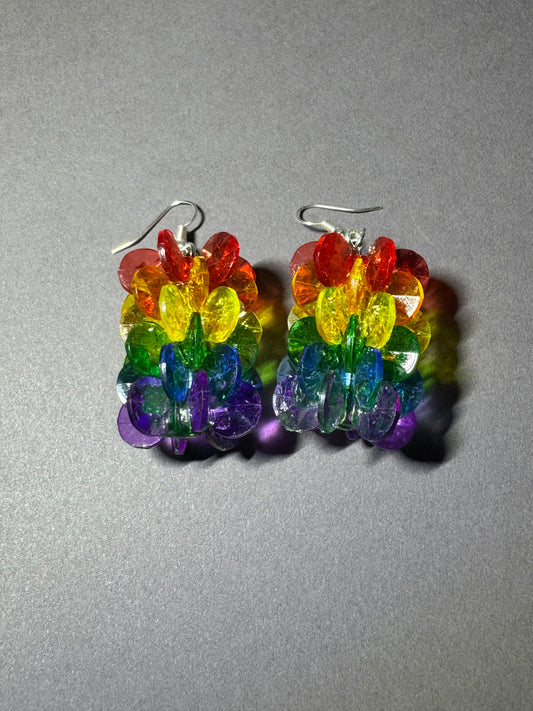 A pair of handmade rainbow beaded dangle earrings with silver fishhook wires, displayed on a textured gray background.
