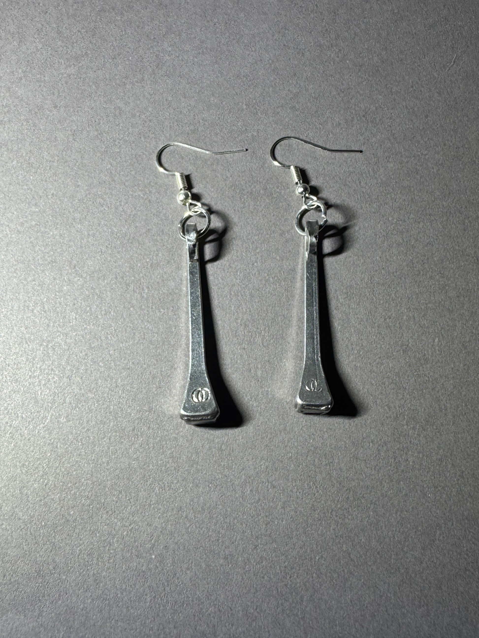 A pair of silver-toned drop earrings with elongated rectangular pendants and fishhook ear wires, photographed on a plain gray surface.