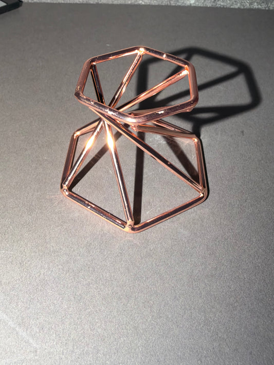A geometric copper wire sculpture on a gray surface with a strong shadow.