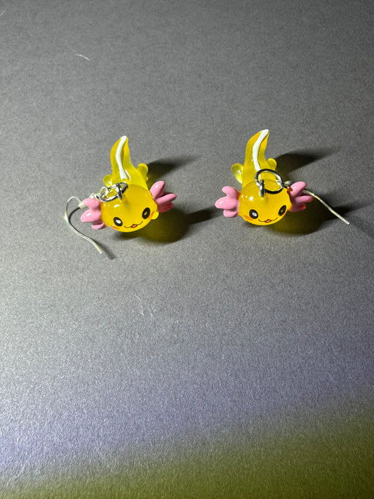 A pair of small yellow and pink fish-shaped earrings with silver hooks, displayed on a gray surface.