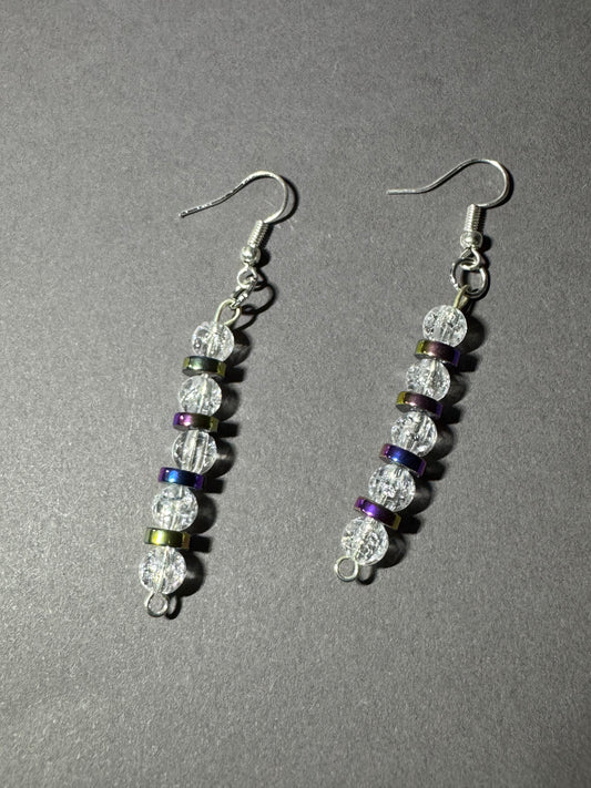 A pair of silver-tone dangle earrings with faceted clear beads and small iridescent spacer beads in green, purple, and blue, displayed on a textured gray background.