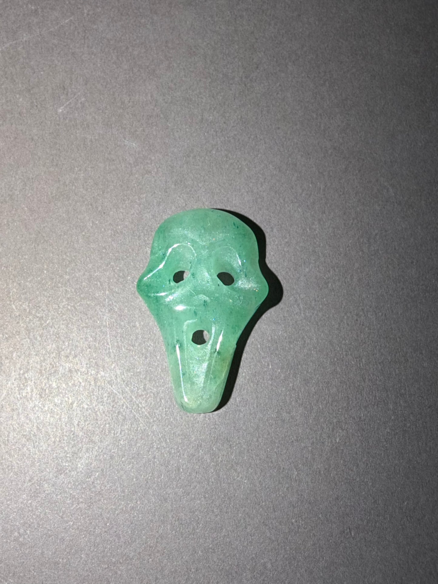 A small carved green stone shaped like a ghost face, photographed on a plain gray background.