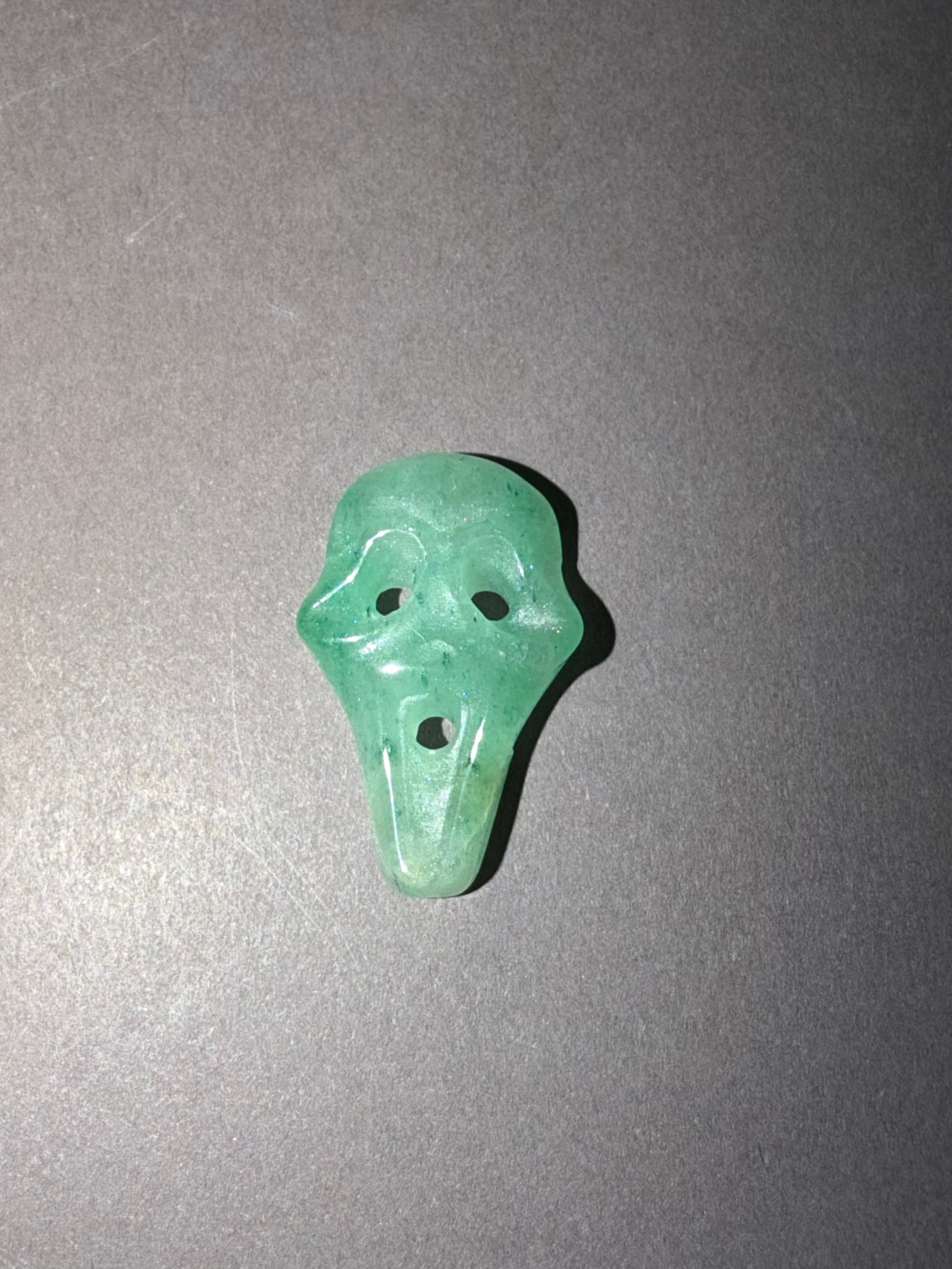 A small carved green stone shaped like a ghost face, photographed on a plain gray background.