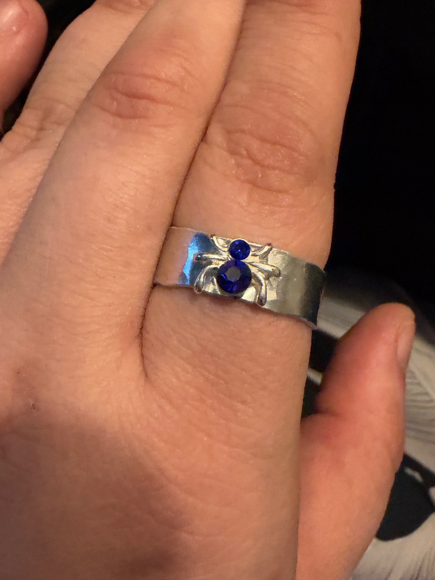 A close-up of a hand wearing a silver ring  blue spider gemstones set into a textured band.