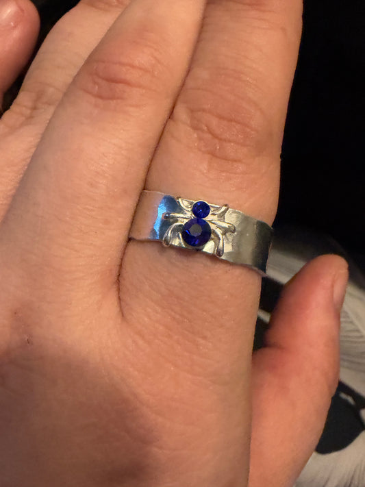 A close-up of a hand wearing a silver ring  blue spider gemstones set into a textured band.