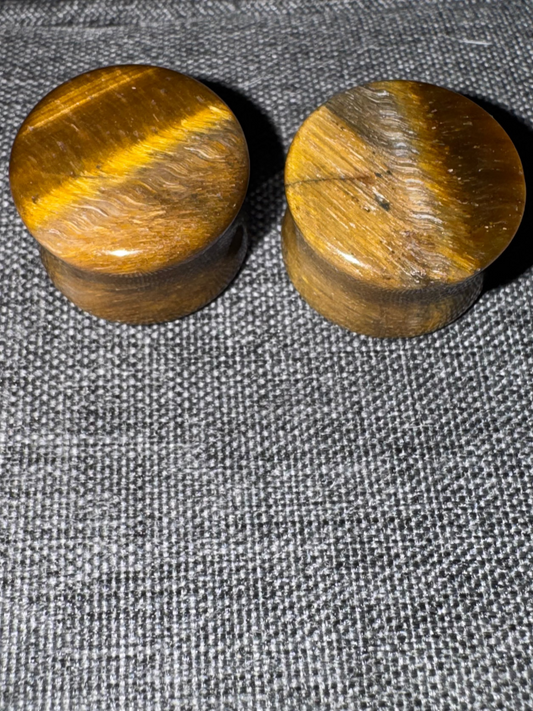 Two wooden tiger eye plugs on a textured gray surface