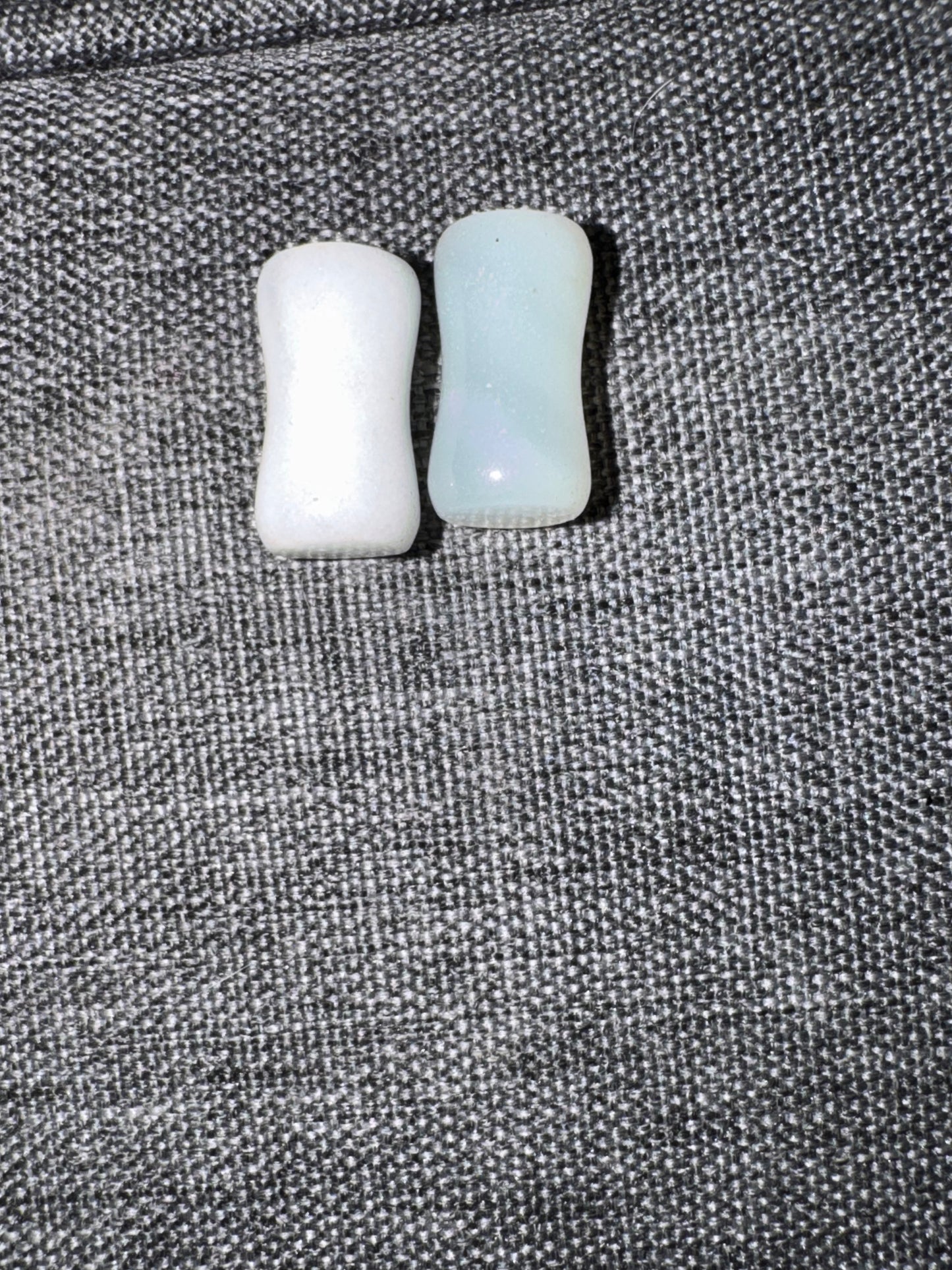 Two small cylindrical objects, one white and one light blue, on a textured gray surface.