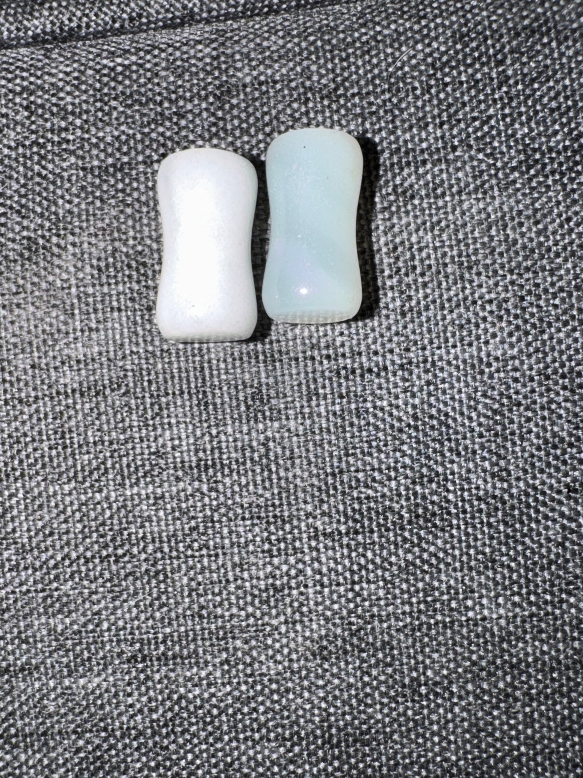 Two small cylindrical objects, one white and one light blue, on a textured gray surface.