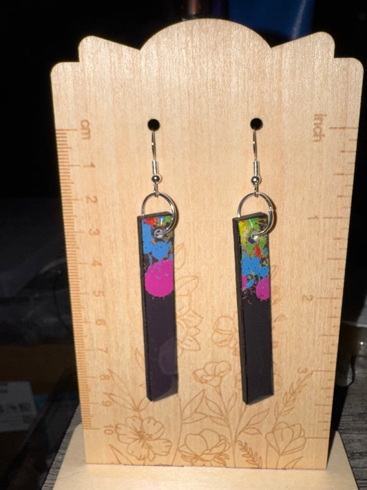 Pair of earrings on a wooden display stand with floral patterns.