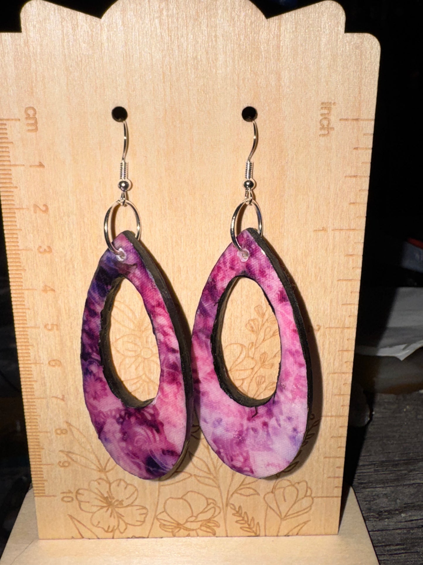 Pair of purple and pink marbled earrings on a wooden display card with floral designs.