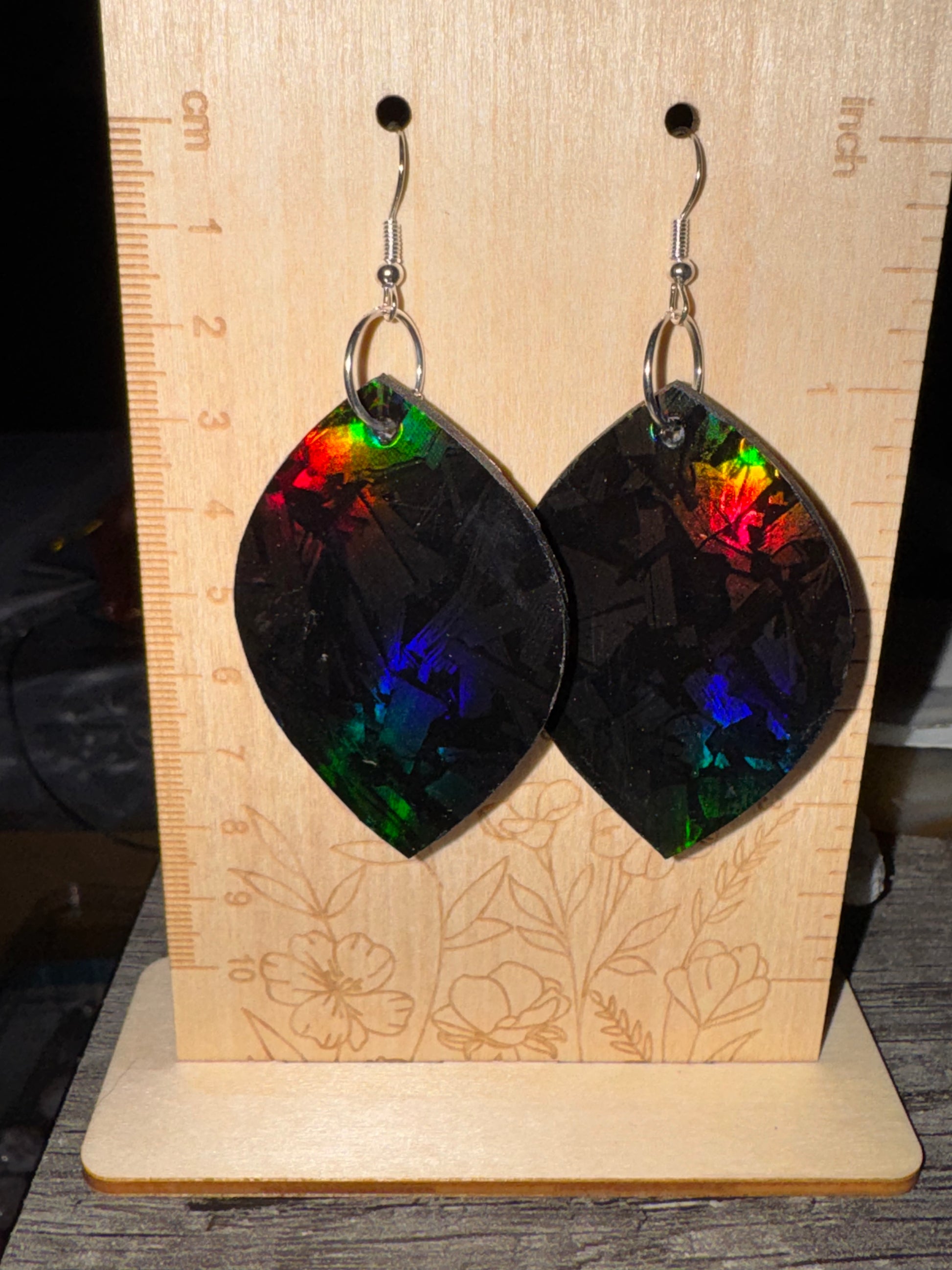 Multicolored leaf-shaped earrings on a wooden stand with floral engraving.