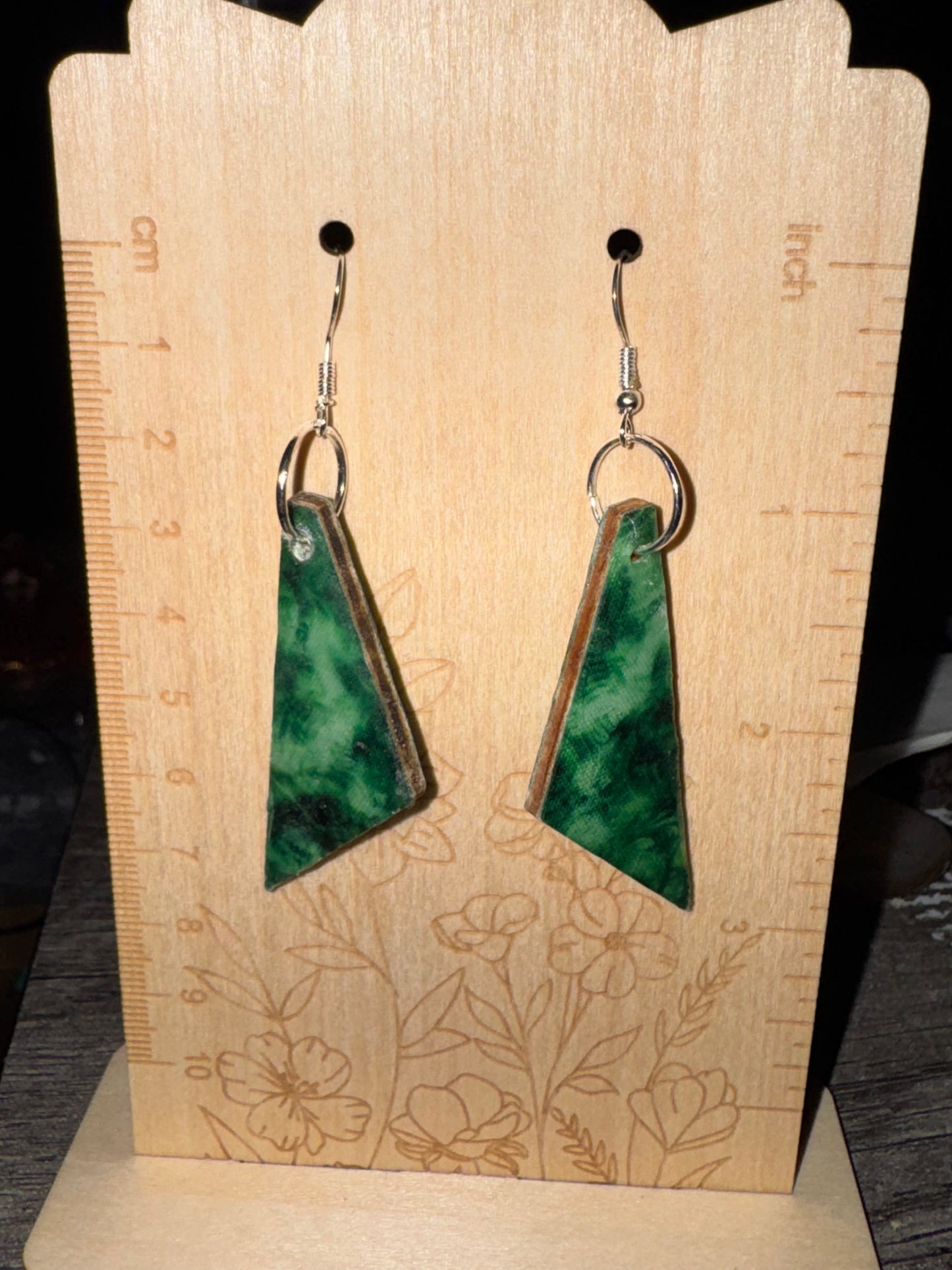 Green triangular earrings on a wooden display with floral designs