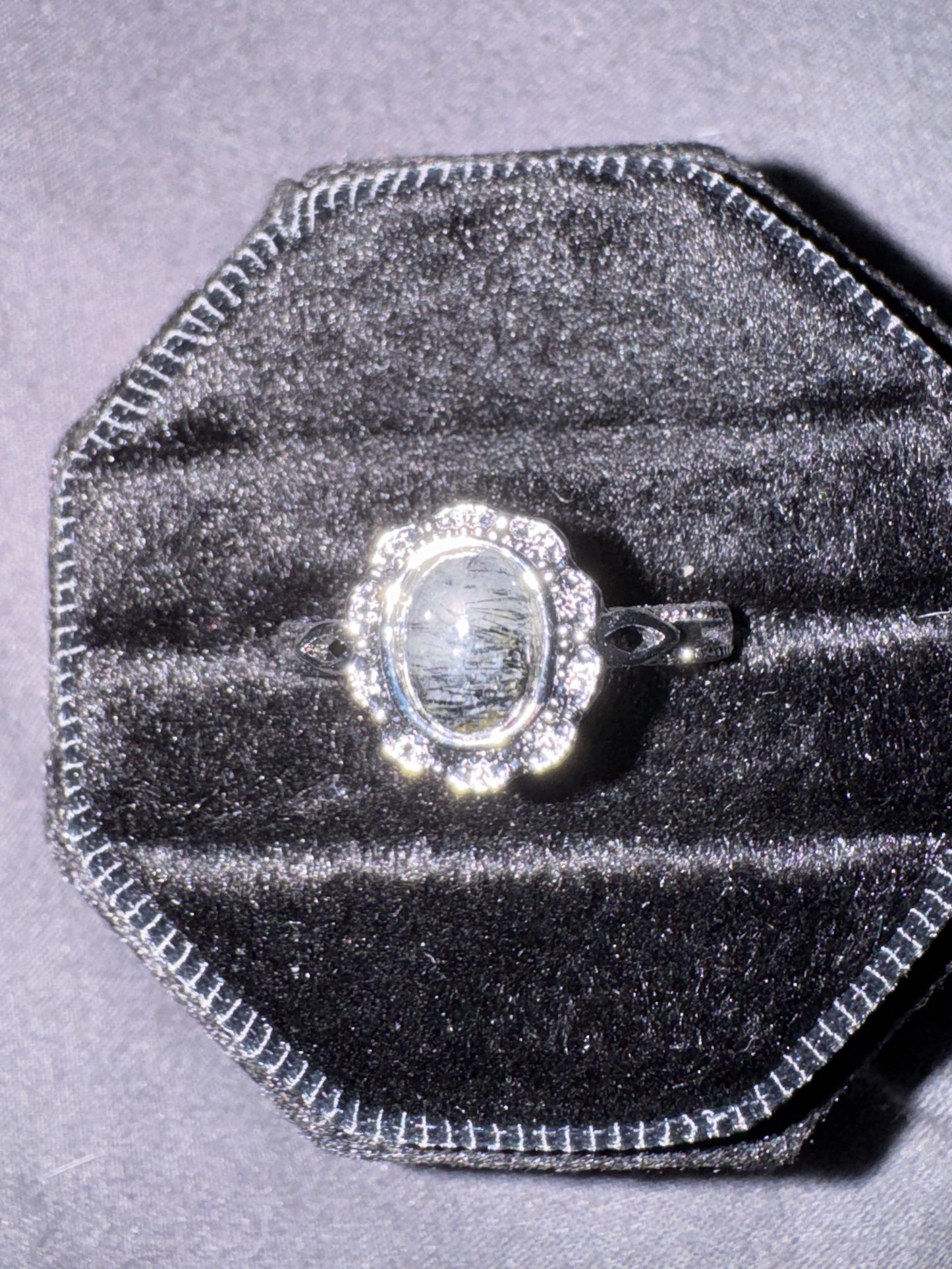 Silver ring with a large central gemstone on a gray velvet cushion