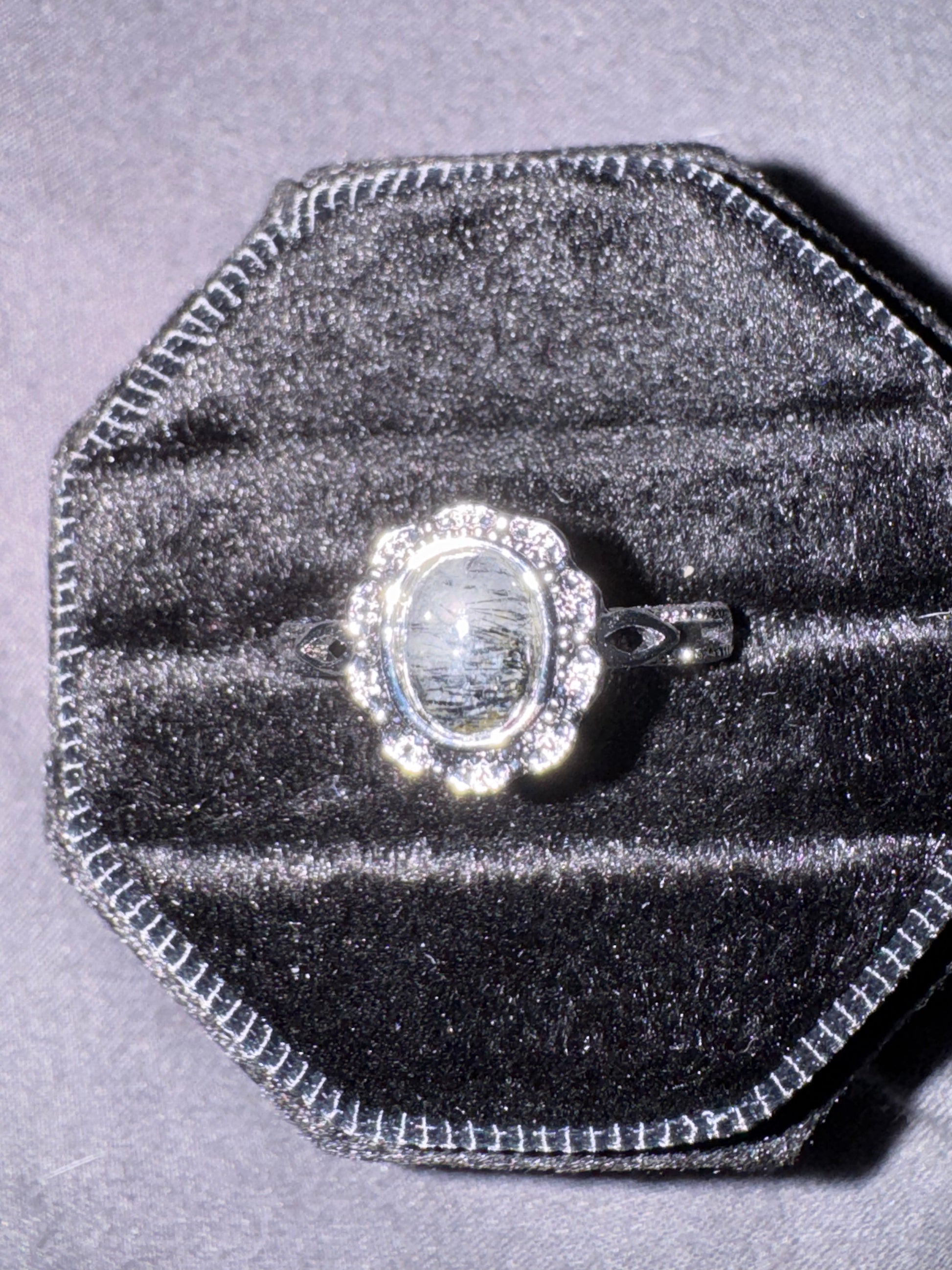Silver ring with a large central gemstone on a gray velvet cushion