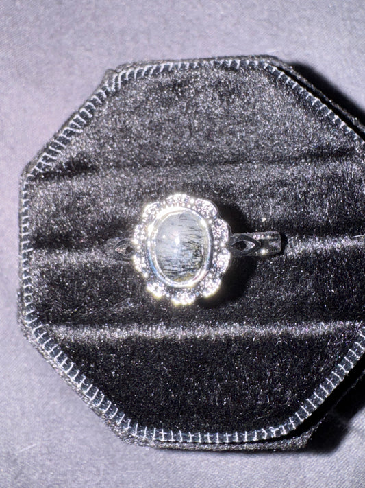 Silver ring with a large central gemstone on a gray velvet cushion