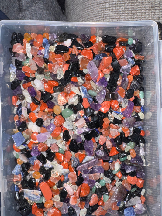 Assorted colored gemstones in a clear plastic container.