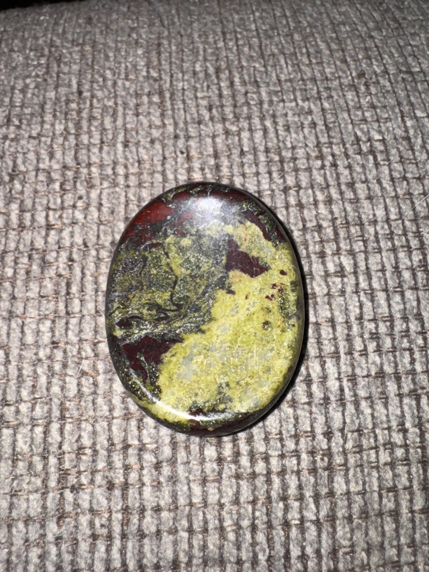 Oval-shaped gemstone with green and red hues on a textured fabric background