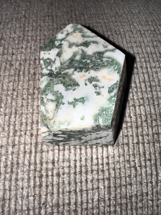 Hexagonal crystal with green and white patterns on a textured surface