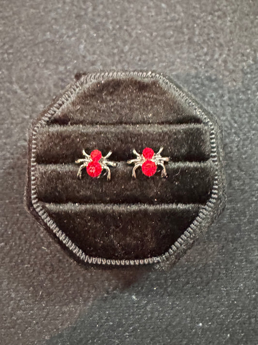 Red spider earrings in a black velvet jewelry bag on a textured gray background