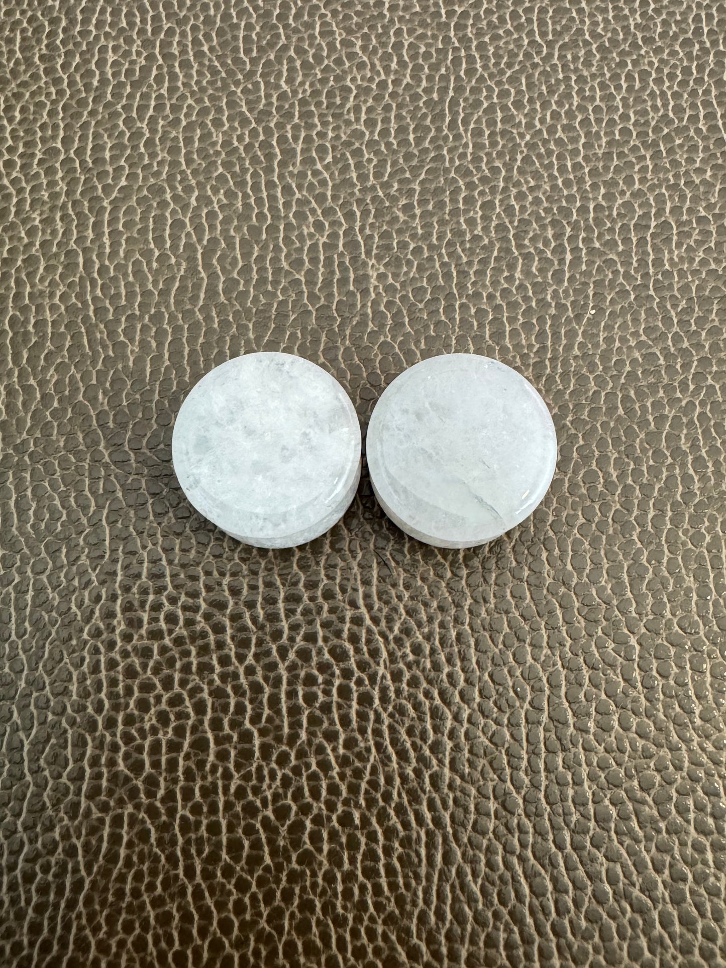 Two white jade ear gauges on a textured  surface