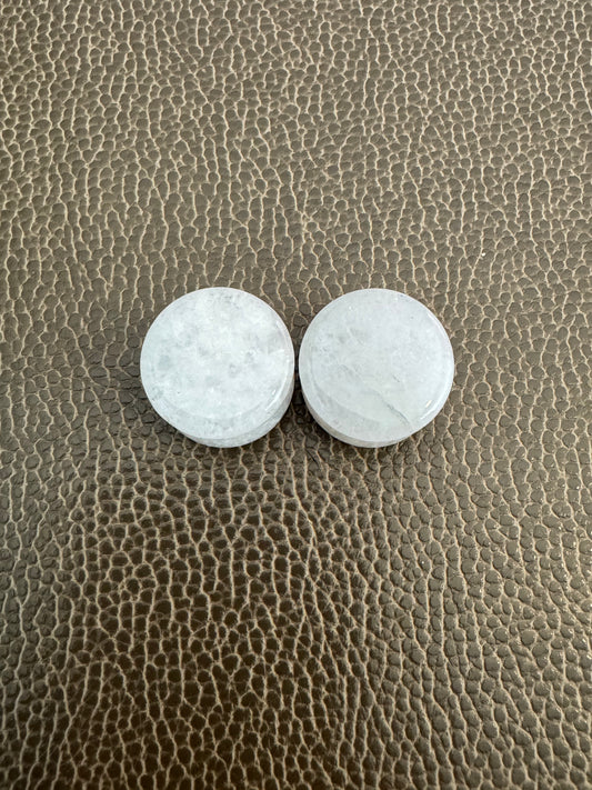 Two white jade ear gauges on a textured  surface