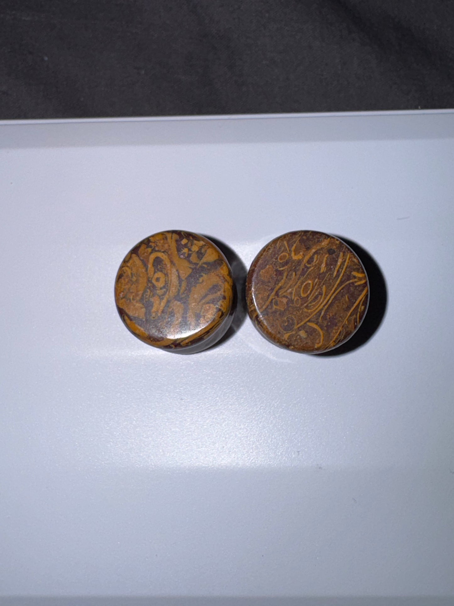 Two round brown ear gauges  with intricate patterns on a white surface.