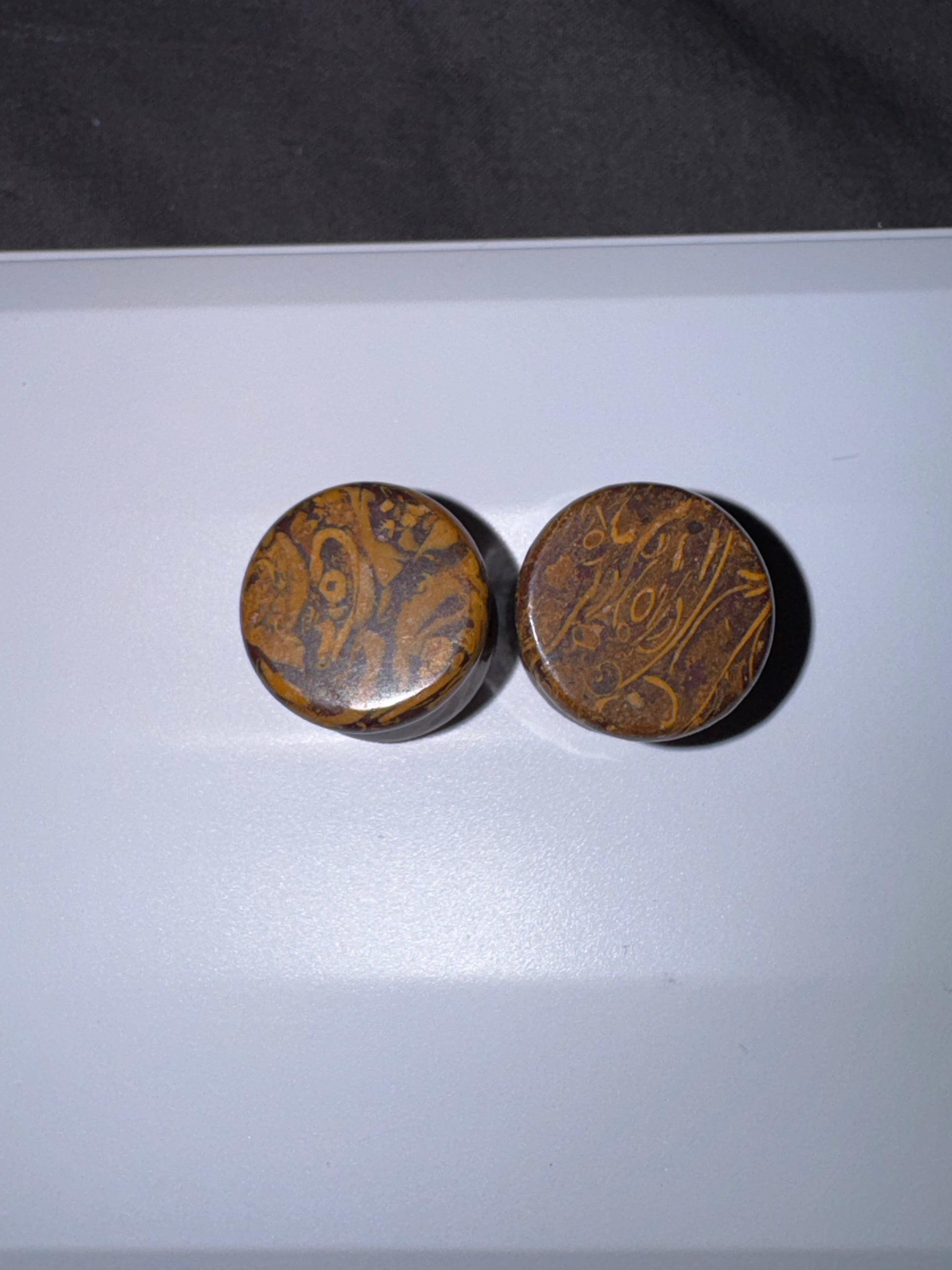 Two round brown ear gauges  with intricate patterns on a white surface.