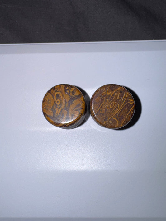 Two round brown ear gauges  with intricate patterns on a white surface.
